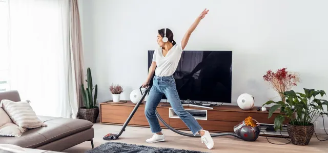 A young woman vacuuming her apartment with headphones on and dancing.